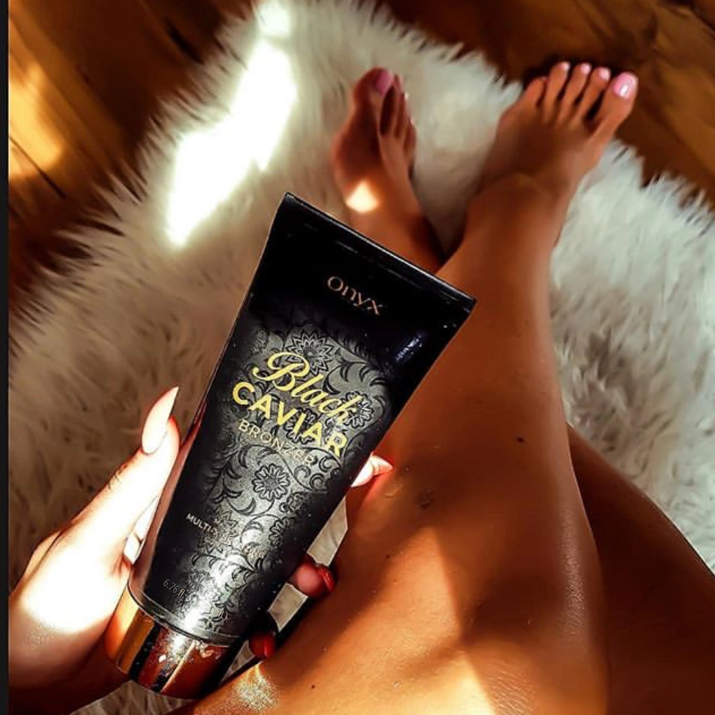 Eine Hand hält die Tube Onyx Black Caviar Lotion, im Hintergrund sind gebräunte Beine auf einem weißen Fellteppich zu sehen