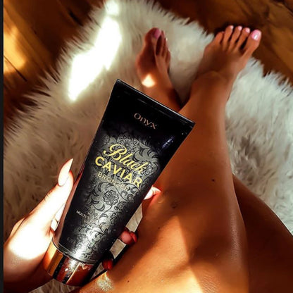 Eine Hand hält die Tube Onyx Black Caviar Lotion, im Hintergrund sind gebräunte Beine auf einem weißen Fellteppich zu sehen