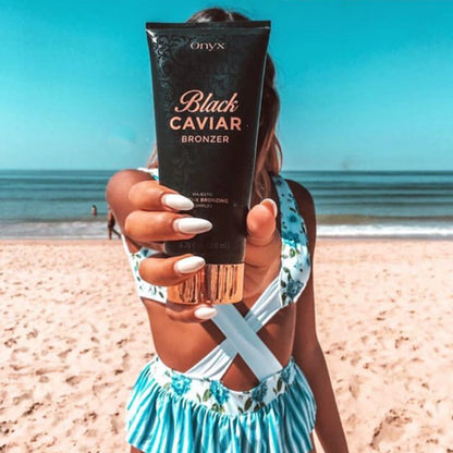 Frau im blauen Badeanzug steht am Strand und hält die Tube Onyx Black Caviar Lotion in Richtung Kamera, im Hintergrund das Meer