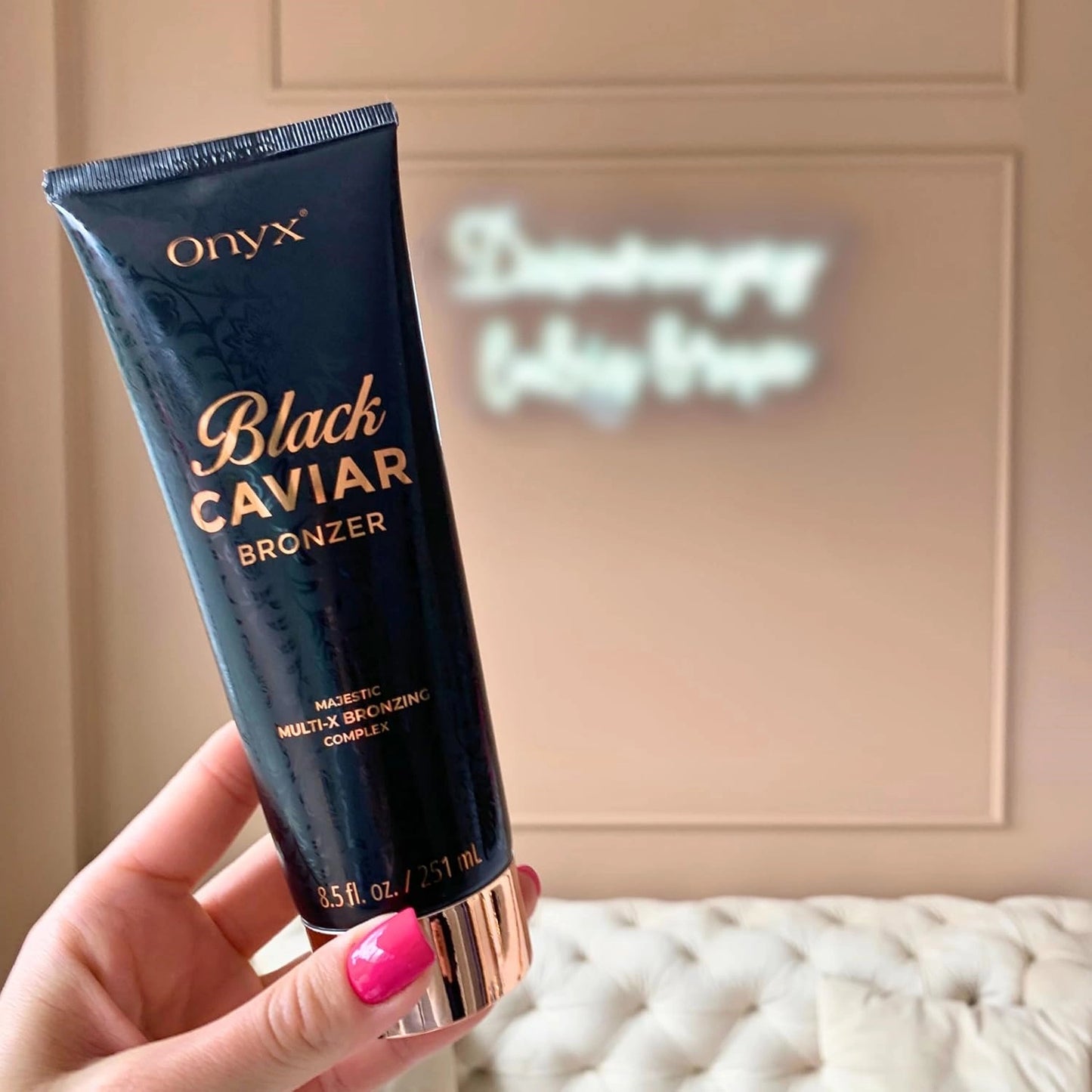 Bräunungscreme fürs Solarium, Hand mit rosa Maniküre hält die Onyx Black Caviar Tube im Zimmer