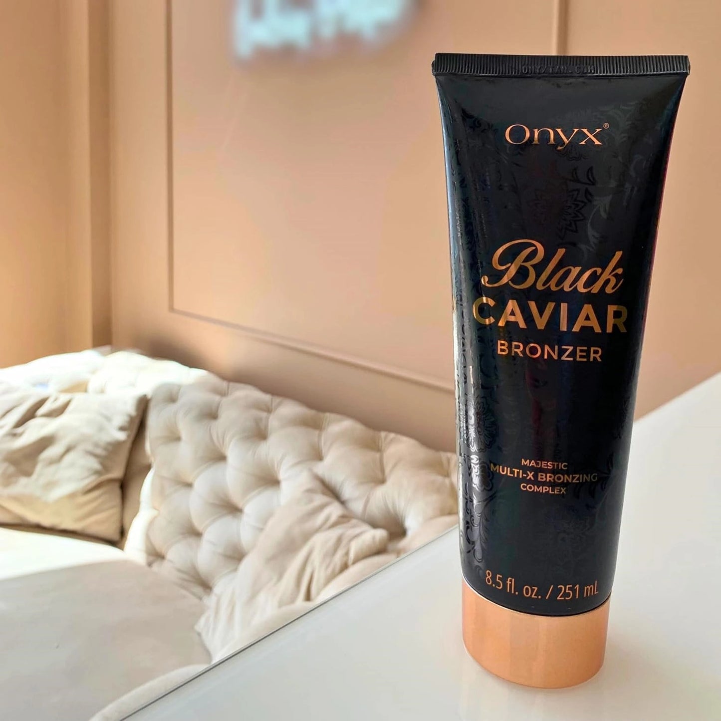Sonnenbank Bräunungscreme, Onyx Black Caviar Tube steht auf weißer Fläche vor beigem Sofa