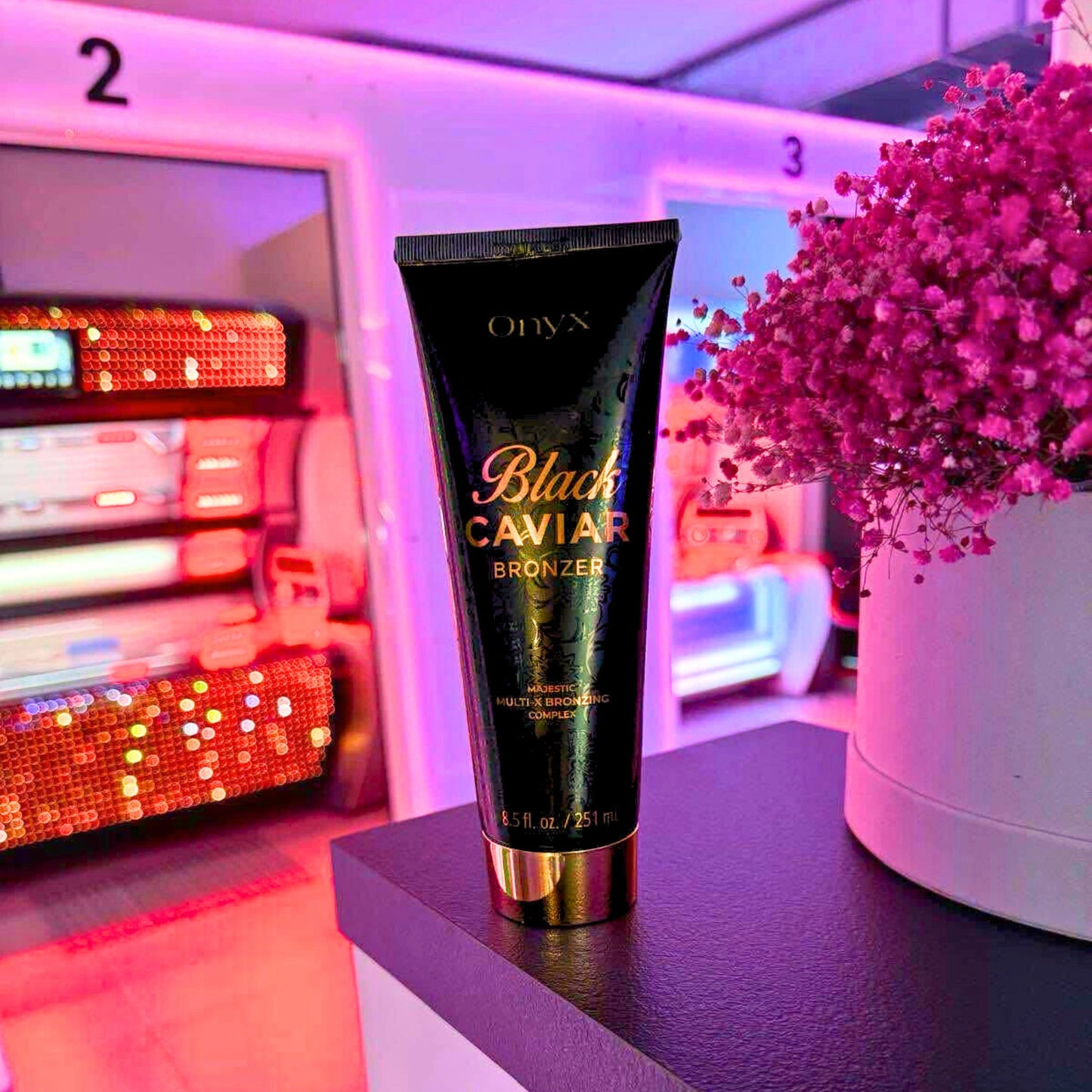 Sonnenbank Bronzer, Onyx Black Caviar Tube steht auf Tresen, im Hintergrund Kabinen mit rosa Licht