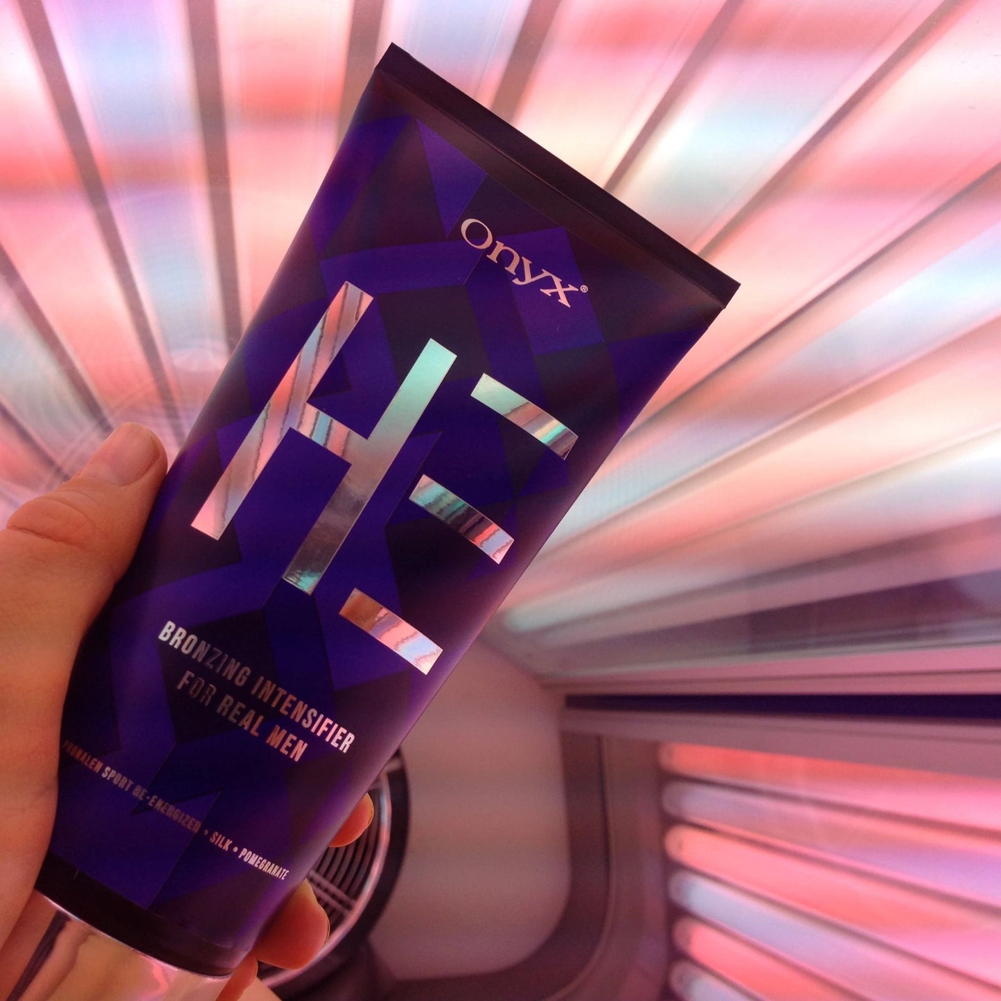 Eine Hand hält eine Tube Onyx HE Bräunungsintensivierer vor einem beleuchteten Solariumhintergrund