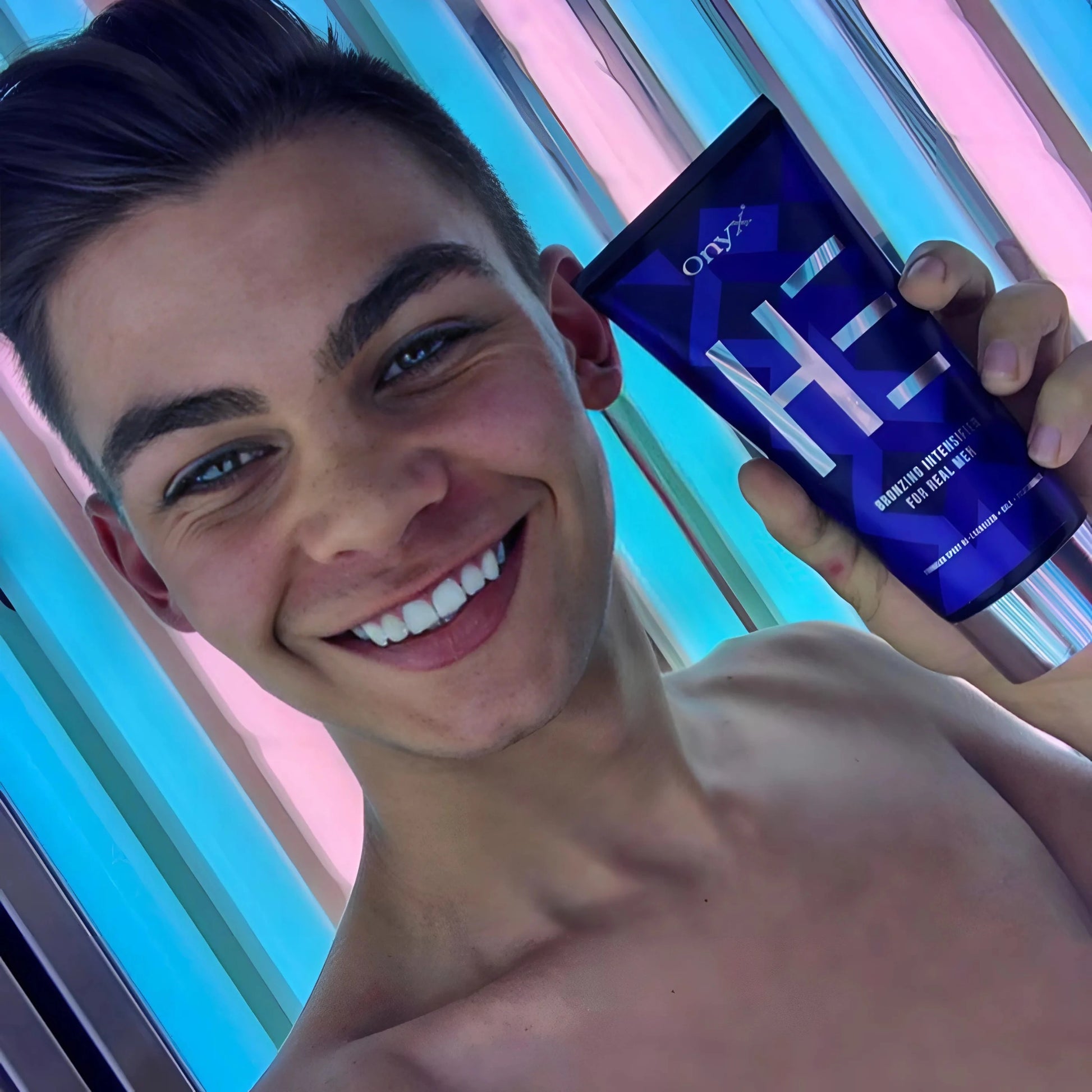 Ein junger Mann macht ein Selfie in einem Solarium und hält eine Tube Onyx HE Bräunungsintensivierer