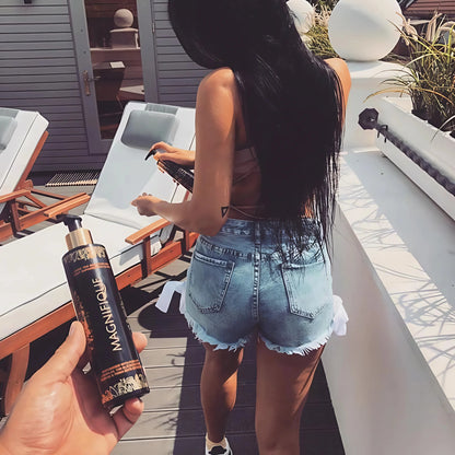 Eine Frau mit langen dunklen Haaren steht auf einer Terrasse in der Sonne und hält Onyx Magnifique Bräunungscreme
