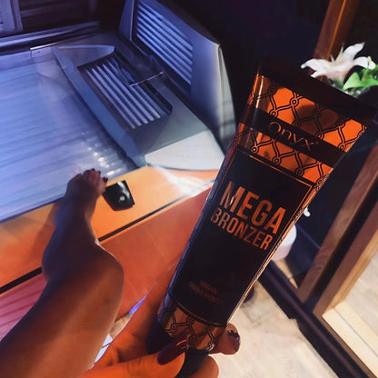 Eine Hand hält eine Tube Onyx Mega Bronzer vor einer geöffneten Sonnenbank mit blauer Beleuchtung