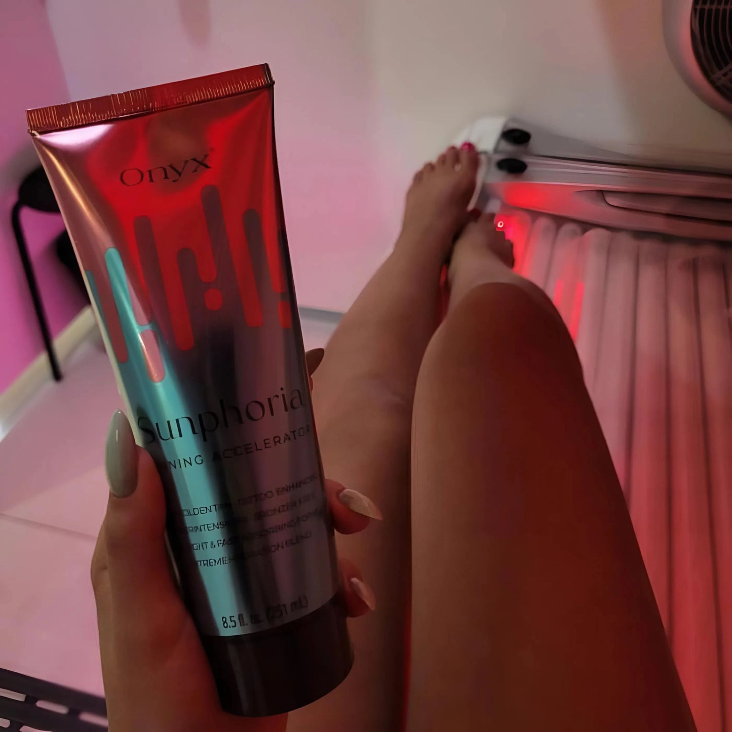 Eine Person liegt in einem Solarium, zeigt ihre gebräunten Beine und hält eine Tube Onyx Sunphoria Bräunungsbeschleuniger