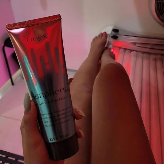 Eine Person liegt in einem Solarium, zeigt ihre gebräunten Beine und hält eine Tube Onyx Sunphoria Bräunungsbeschleuniger