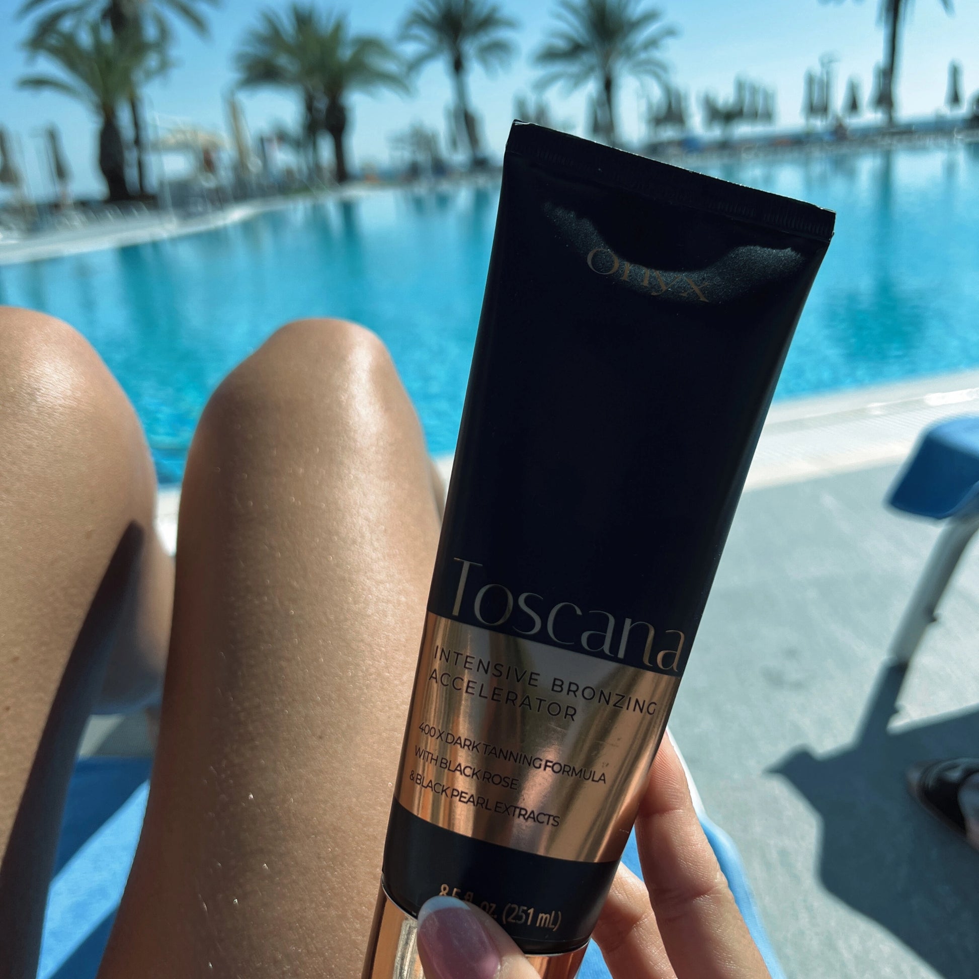 Onyx Toscana Sonnenbank-Creme mit Bronzer wird vor gebräunten Beinen am Pool gehalten
