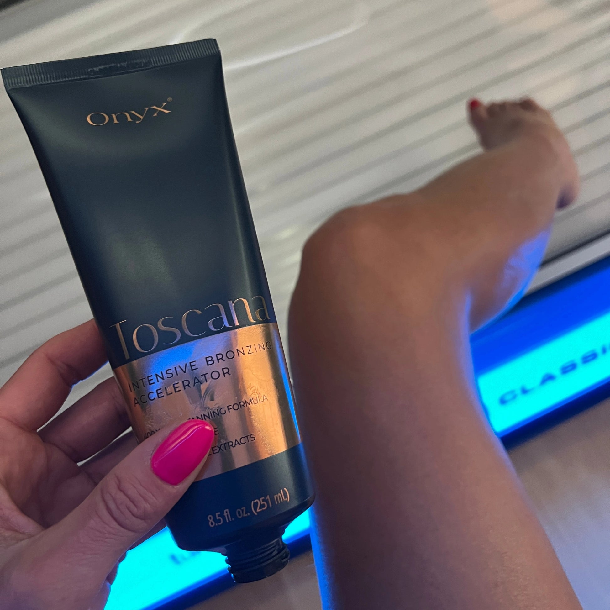 Geöffnete Onyx Toscana Sonnenbank-Bräunungscreme vor Bein im Solarium mit pink lackierten Nägeln